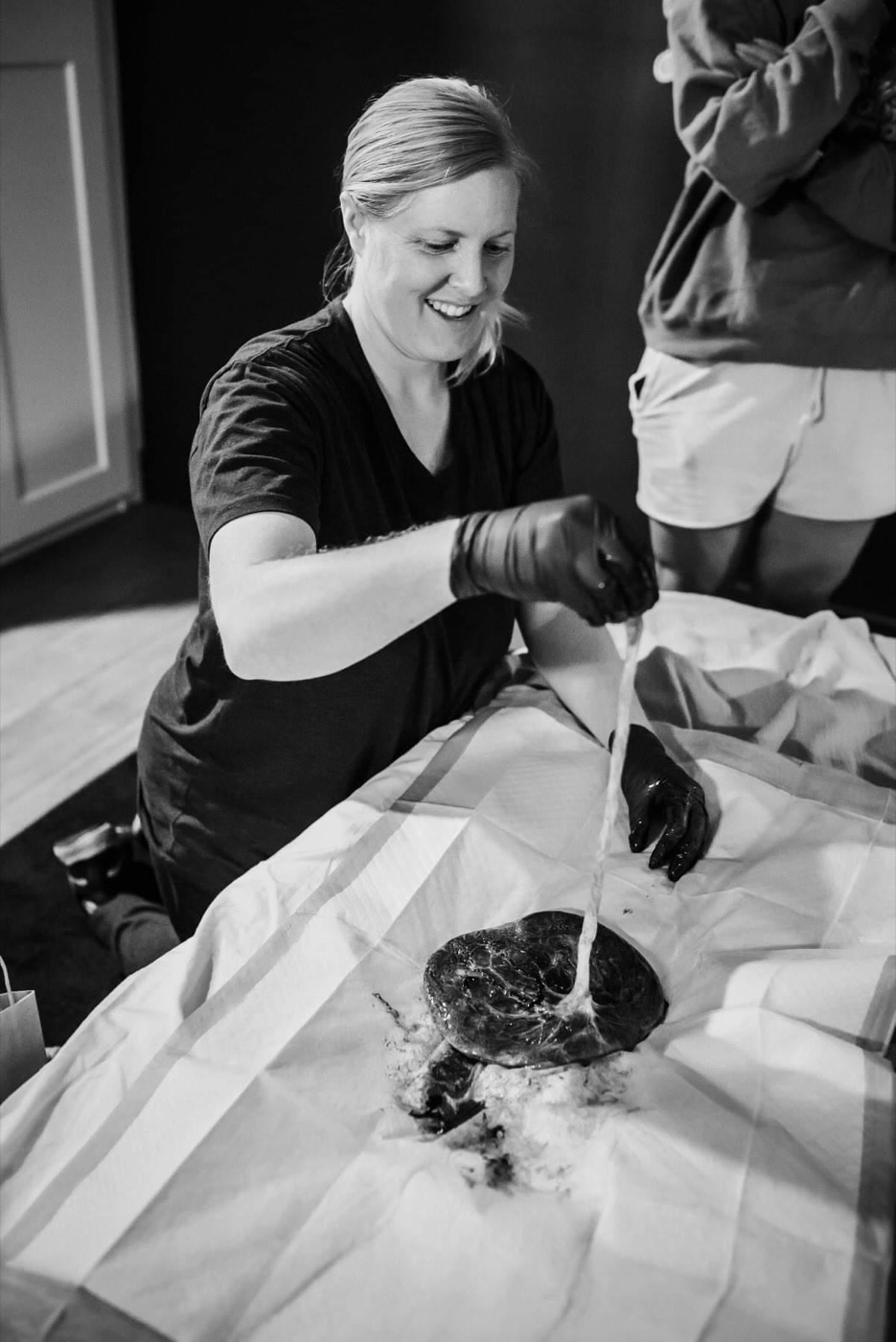 A midwife smiling as she carefully prepares a placenta and cord on a sterile drape